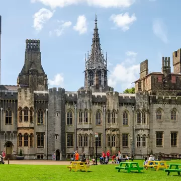 People picnic on the lawns outside a large ornate building: the residential quarters at Cardiff Castle, Wales.
