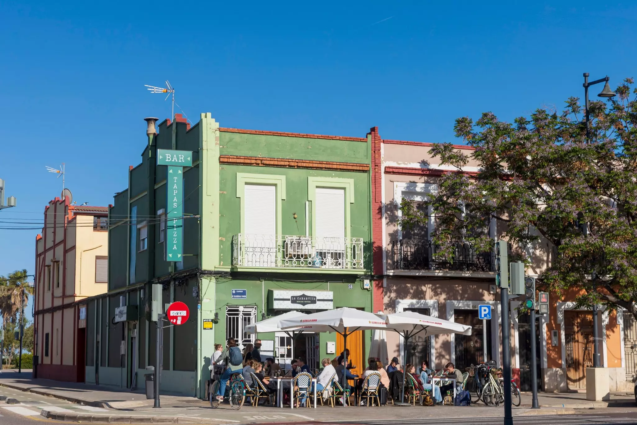 People sit at outdoor tables in front of a restaurant in a green building.