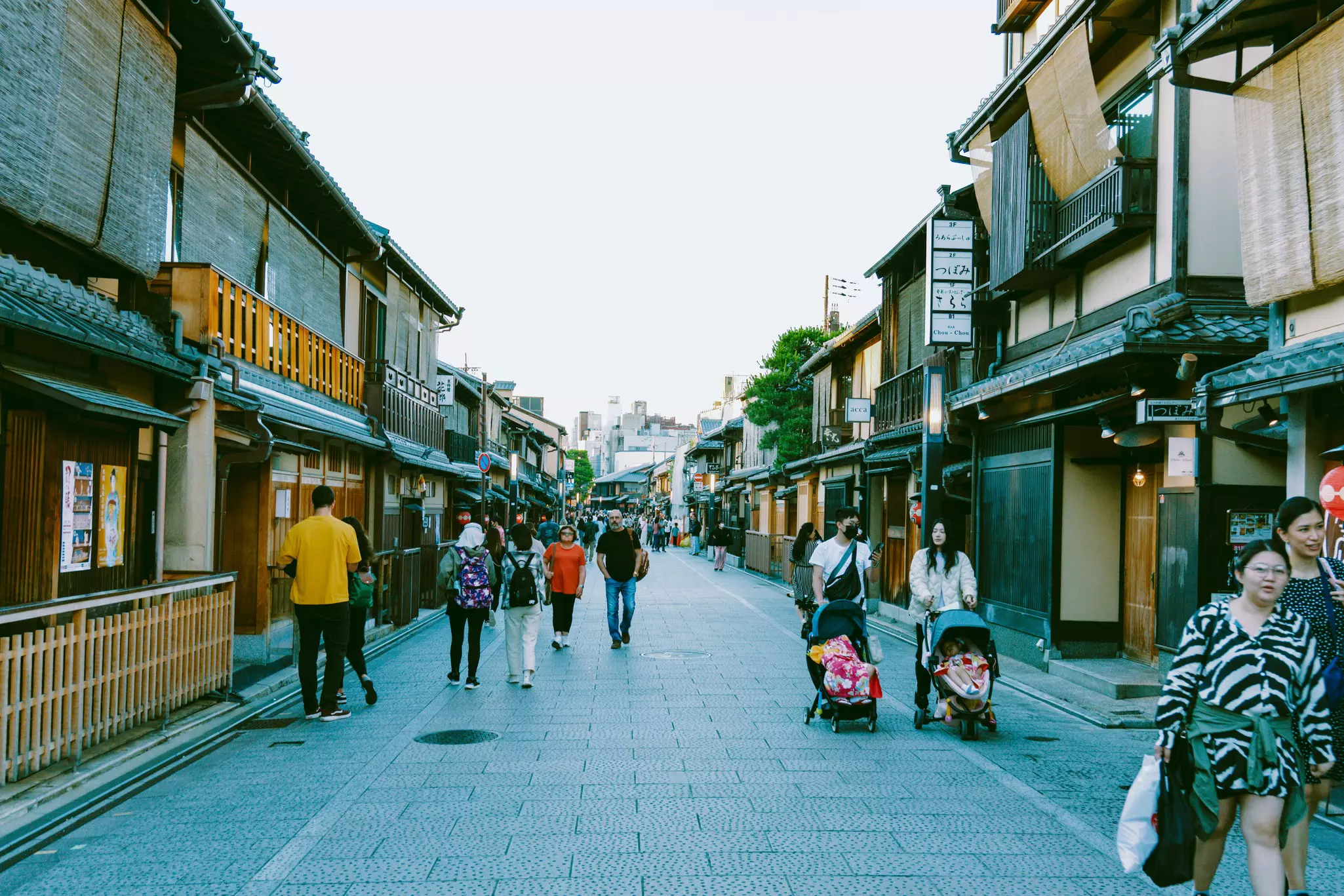 Pedestrials wander through a street in Japan. Two people are pushing strollers with toddlers in them.