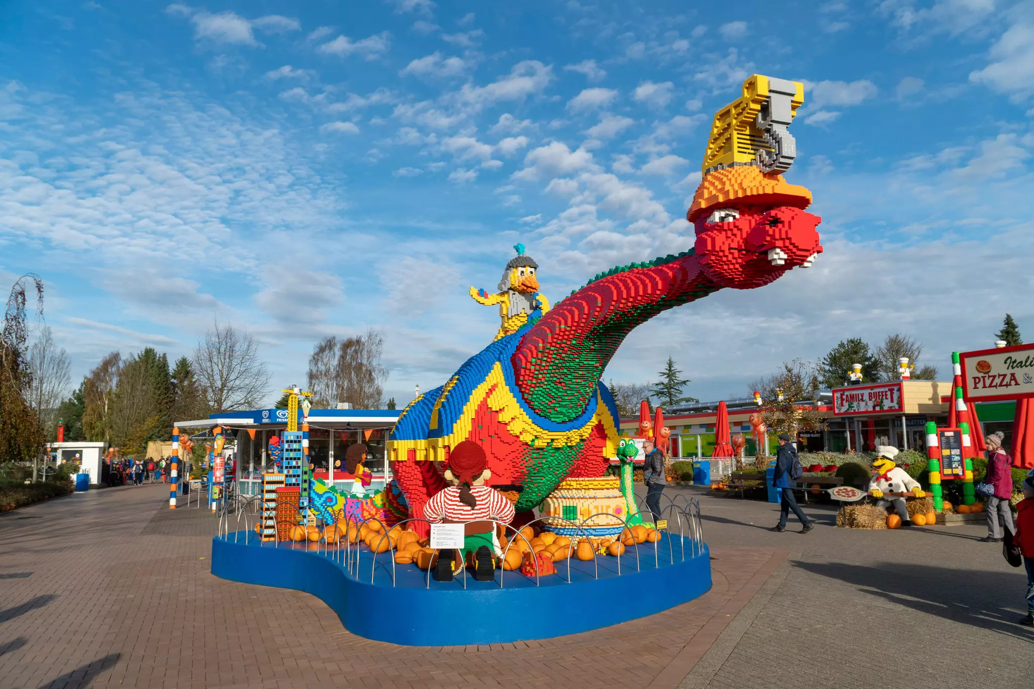 A dragon made from red and green plastic bricks is displayed outdoors at a theme park.