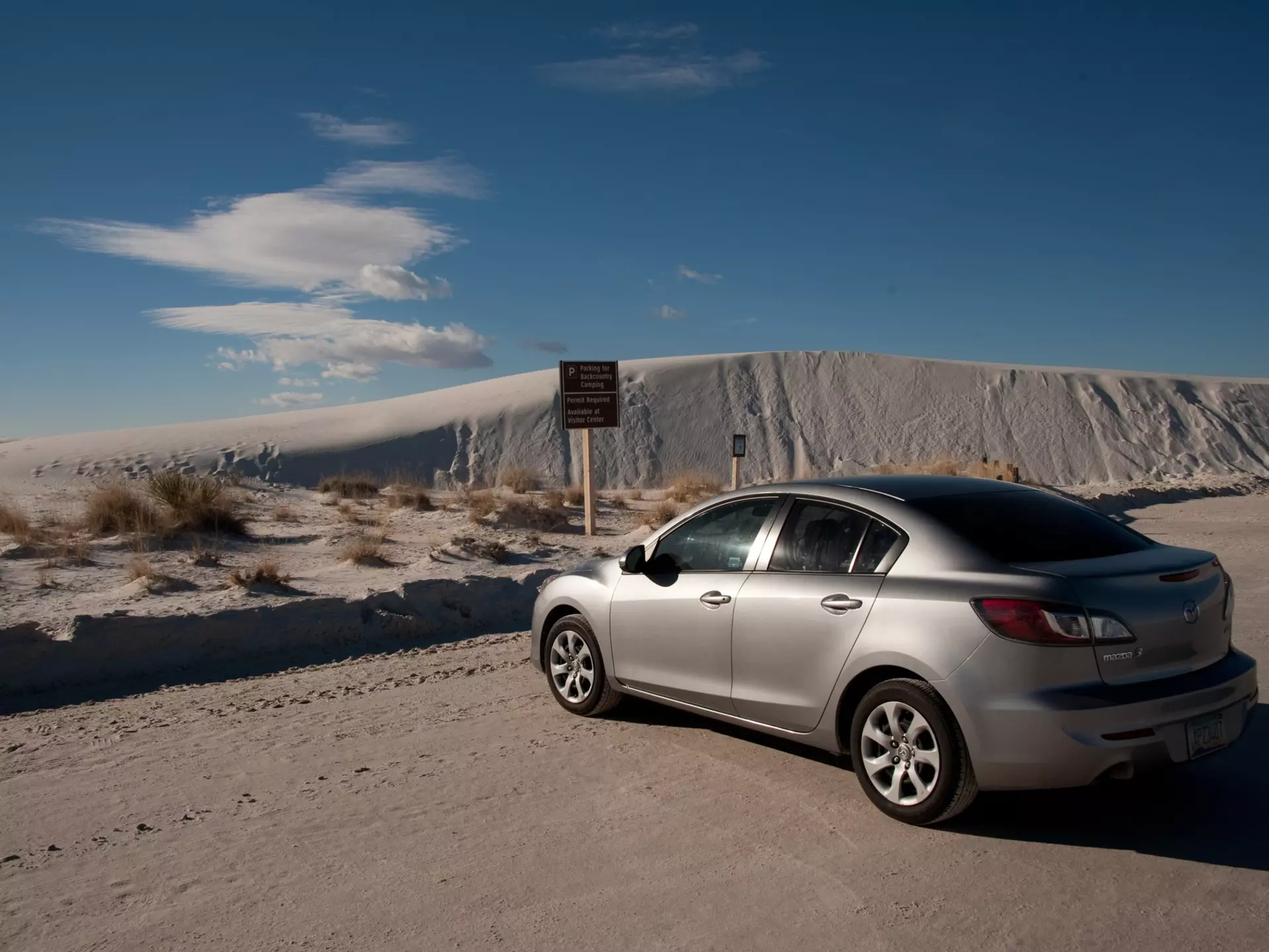 ALAMOGORDO, NEW MEXICO - DECEMBER 9, 2013: A 2013 silver 4-door Mazda 3 sedan Enterprise rental car, parked at the Backcountry Camping Loop parking area, at White Sands National Monument.  License Type: media  Download Time: 2023-09-01T03:35:18.000Z  User: aomi.ito_lonelyplanet  Is Editorial: Yes  purchase_order:   