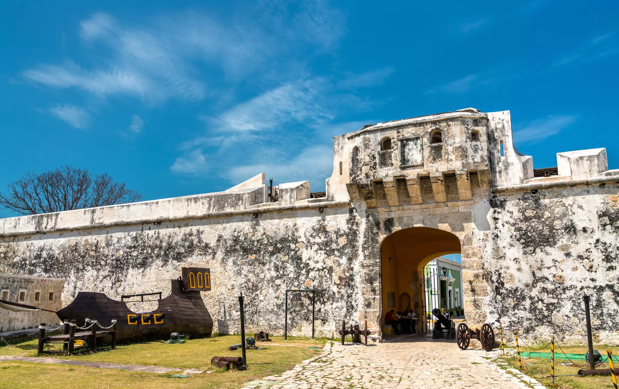 A gateway in ancient city walls with canons standing nearby.