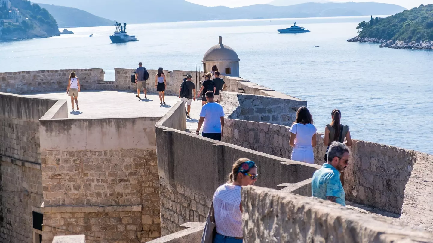 People walking on the city walls of Dubrovnik on a clear day.
