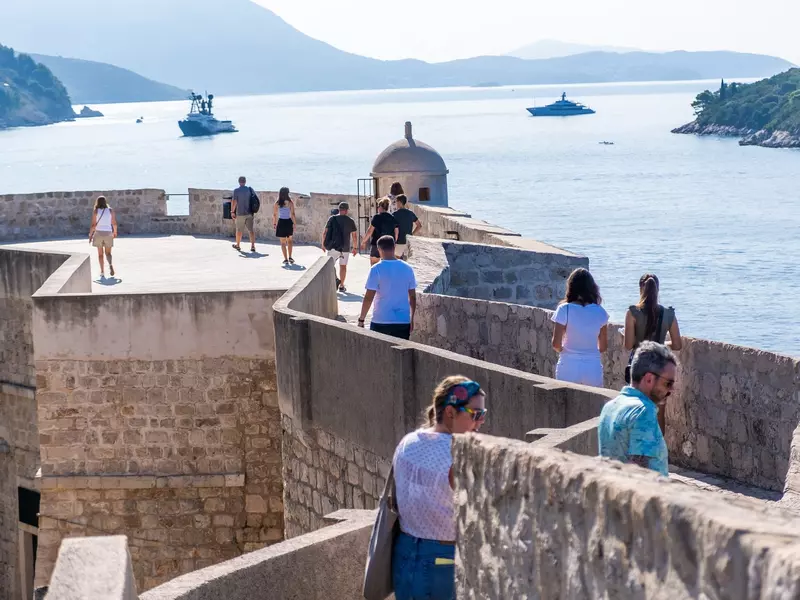 Visitors stroll along the historic Dubrovnik city walls with the sea in the background