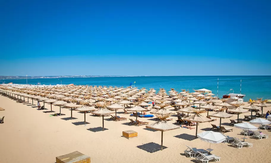 Rows of thatched parasols and sun loungers on a wide sandy beach beside the blue Black Sea near Varna, Bulgaria