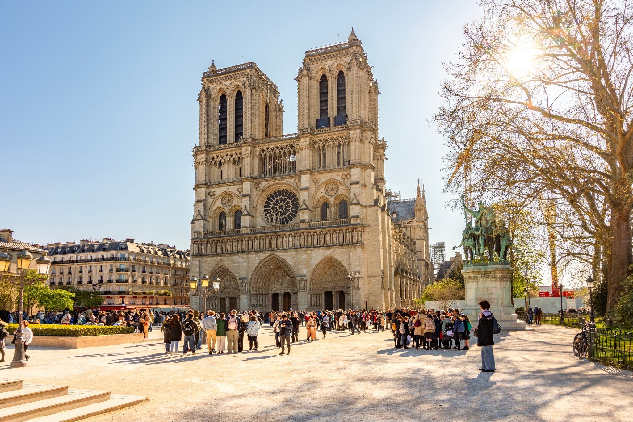 People gather in front of a two-towered cathedral on a sunny day: Cathédrale Notre Dame de Paris, Paris, France.