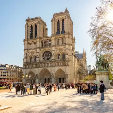 People gather in front of a two-towered cathedral on a sunny day: Cathédrale Notre Dame de Paris, Paris, France.