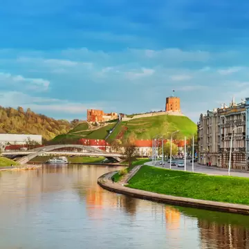 A red-brick castle on the top of a green hill by a river