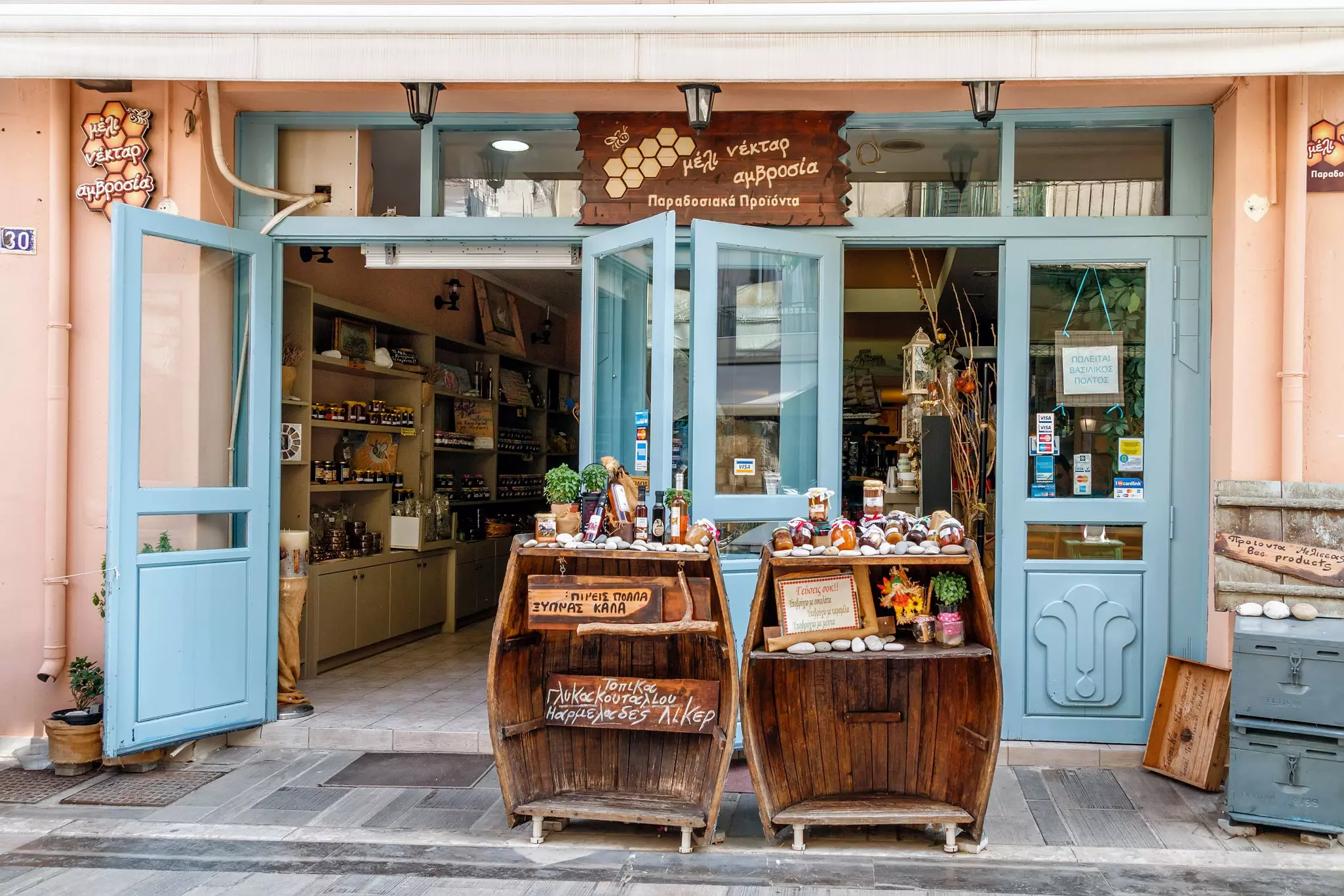 A light blue storefront with two wood tables displaying honey on the sidewalk.
