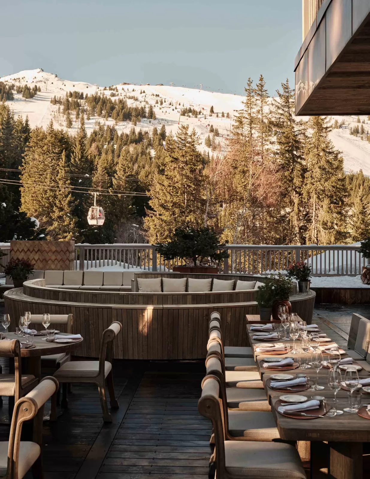 An outdoor dining terrace in a snowy location as a cable car passes by: Rosewood Courchevel 