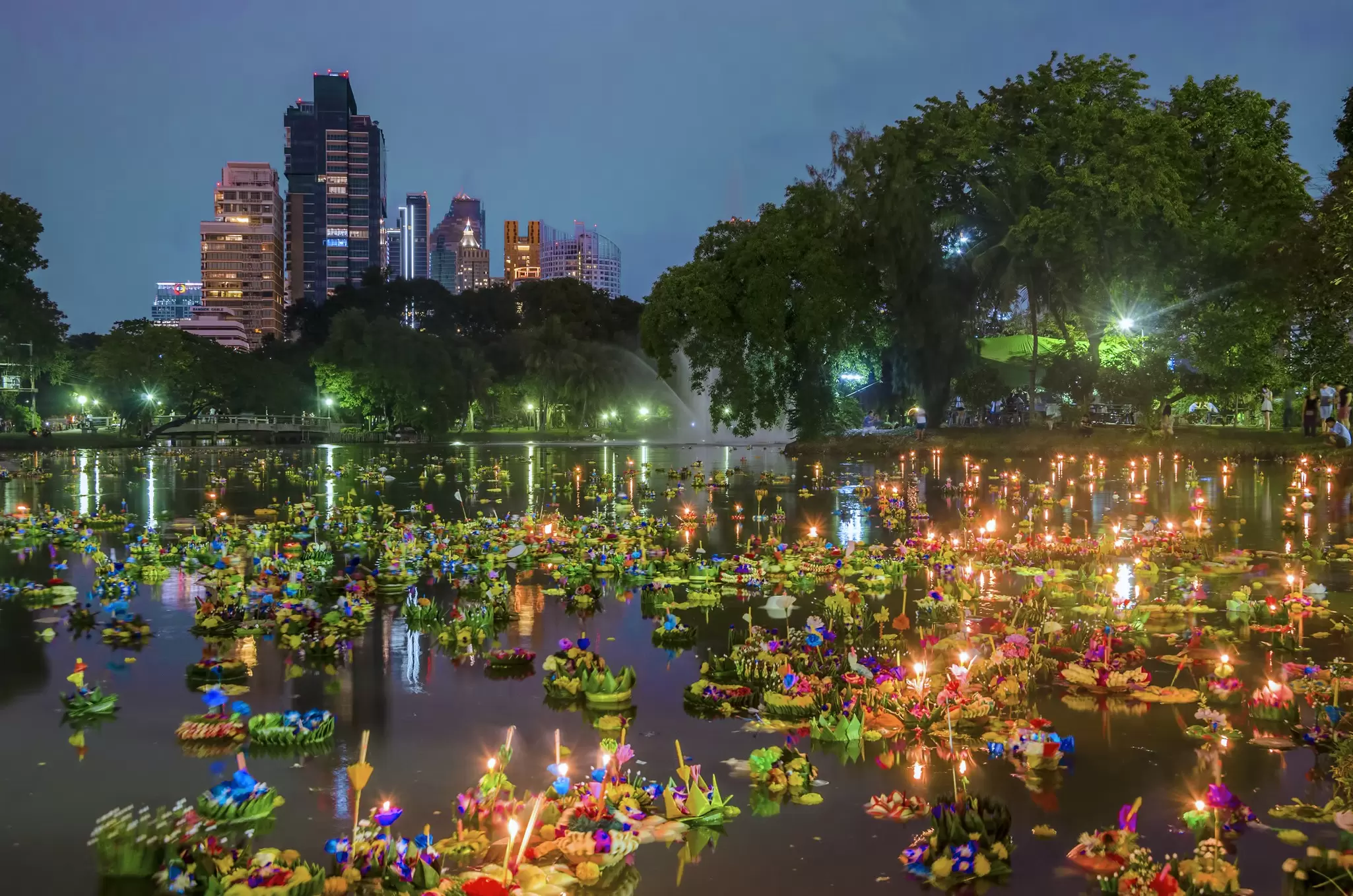 Flowers and lanterns float on a lake with the city skyline visible behind, Bangkok, Thailand