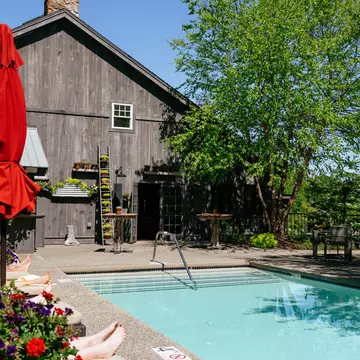 The adults-only pool at Hidden Pond resort in Kennebunkport, Maine. Rectangular pool, adults on lounge chairs, plants against a classic Maine barn-type building. 
