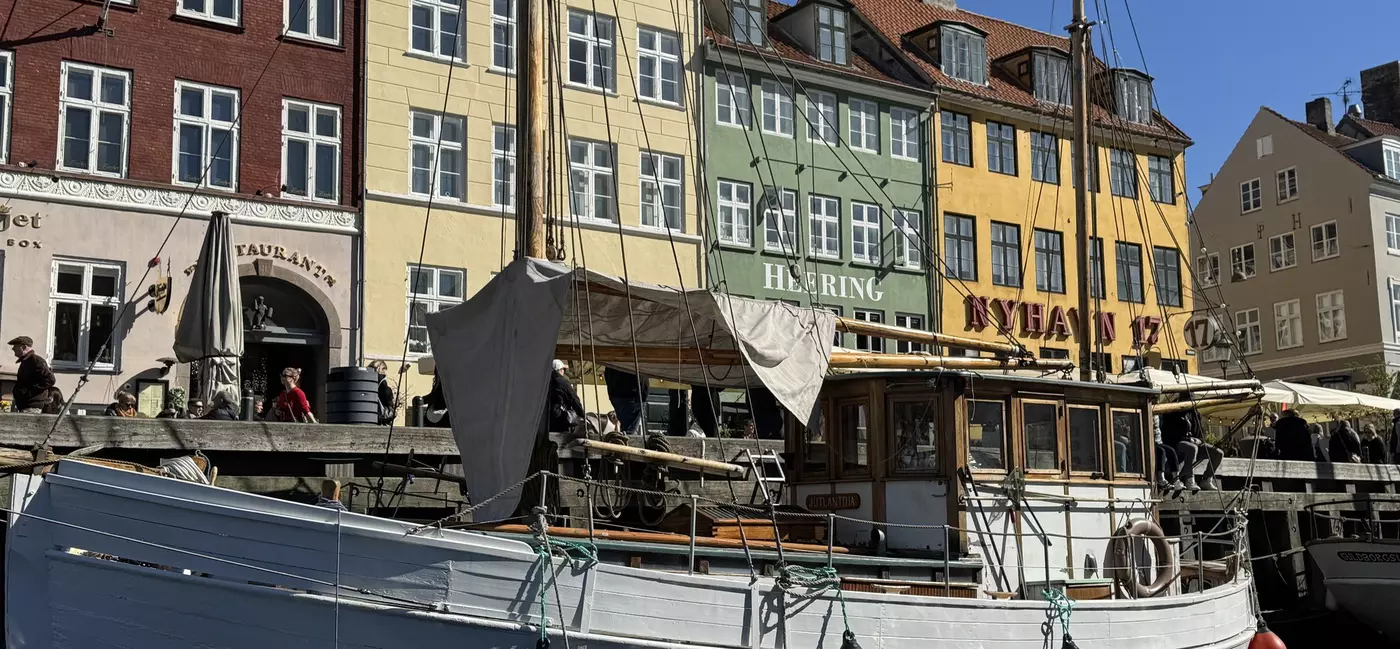 Close-up of white canal boat on the water with colorful brick buildings in the background in Nyhavn, Copenhagen.