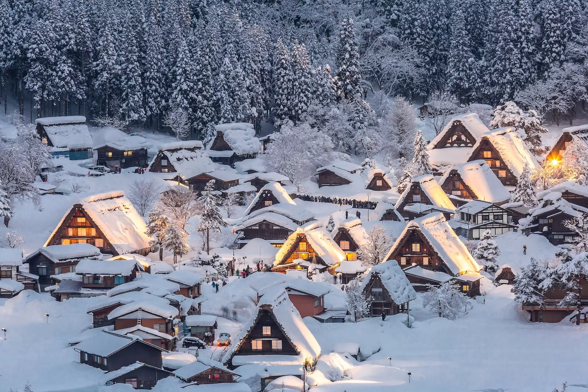 A village of structures with steeply peaked roofs under snowfall in the evening.