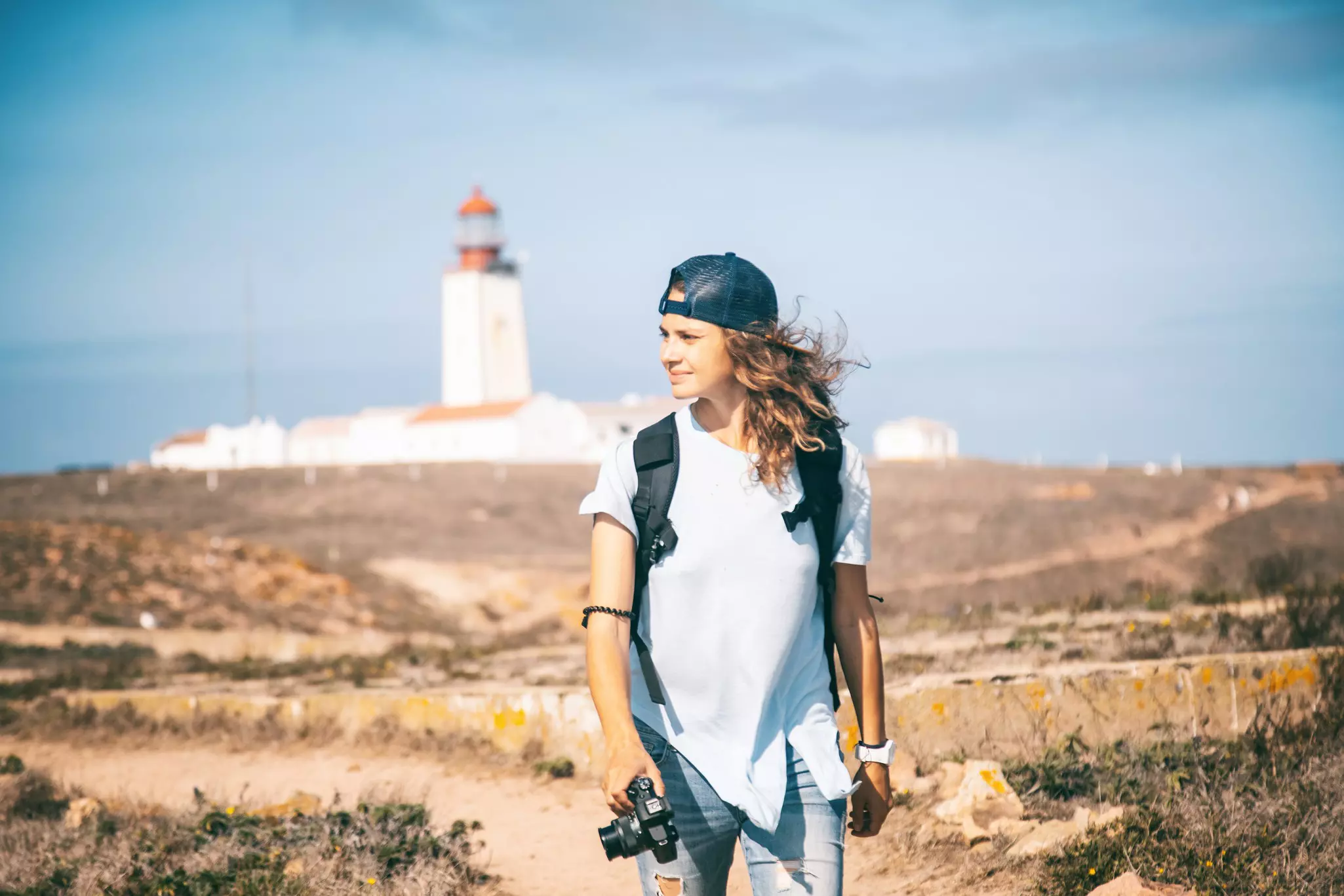 A photographer walks along a trail in a nature reserve with a lighthouse in the background