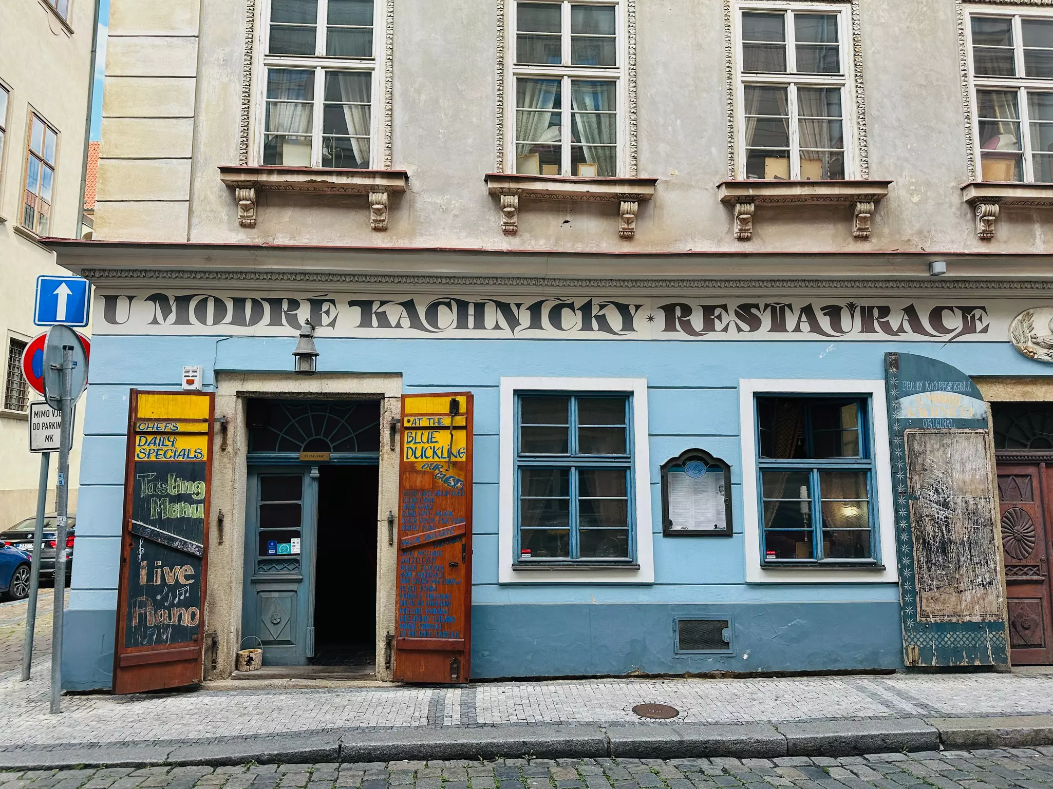 The sky blue facade of a building with "U Modré kachničky Restaurace" painted above the door in dark all-capital letters