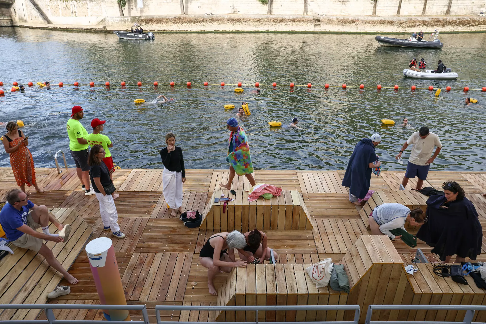 People swim at a cordoned off section of a river with a basic wooden deck area for them to change in and out of their swimwear.