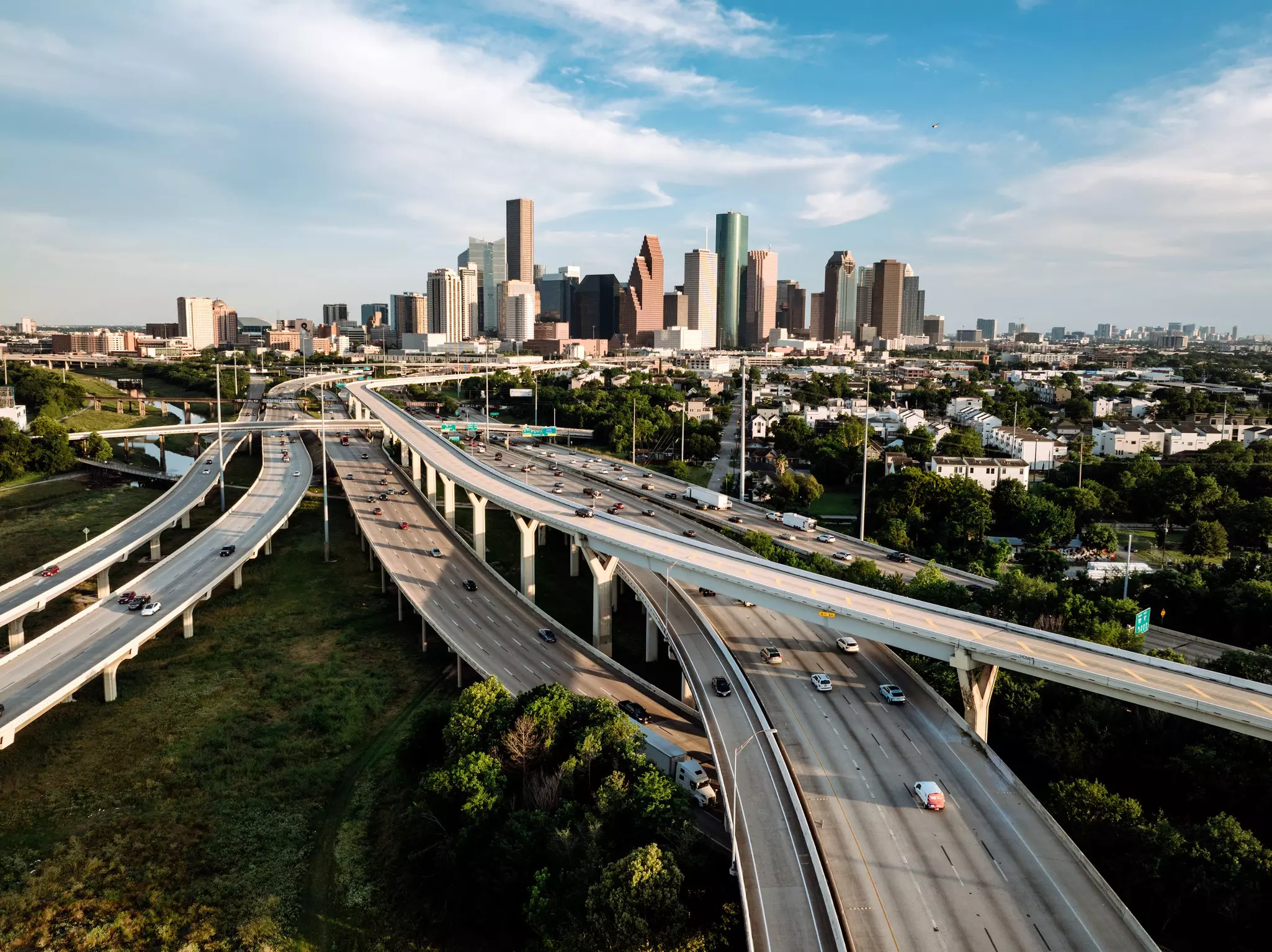 Highways and interstates with cars driving on them converge on the approach to a high-rise city.