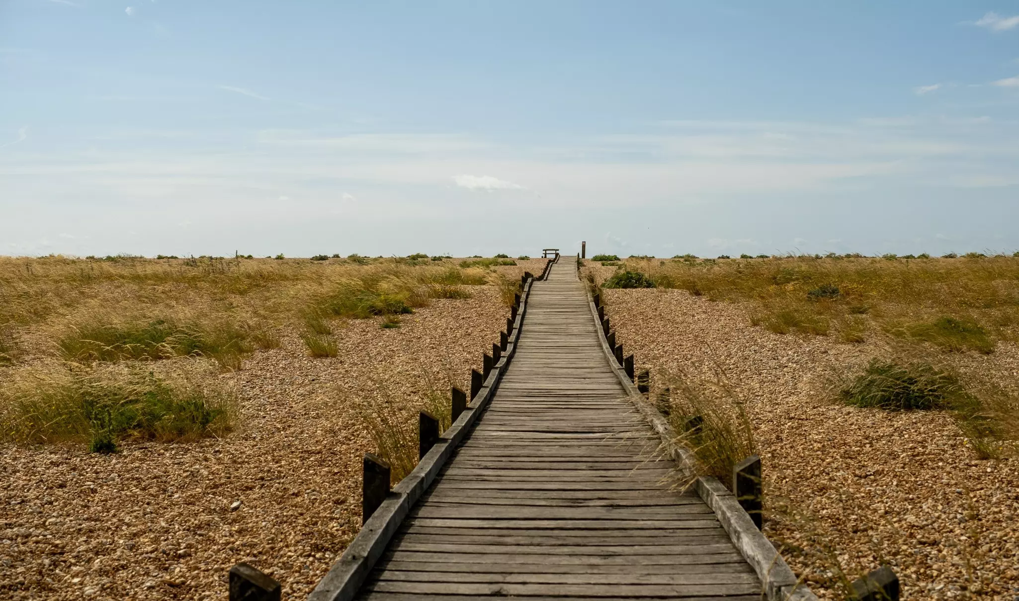 A wooden boardwalk across pebbles and grasses.