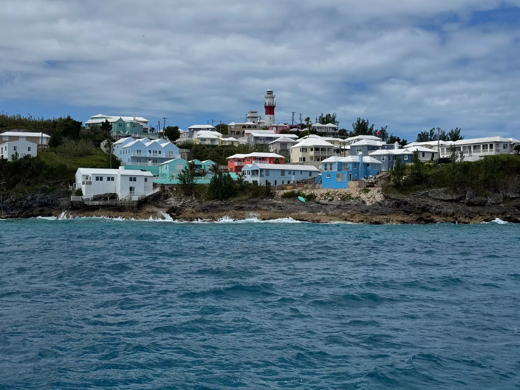 A lighthouse and brightly colored buildings sit beside the ocean.
