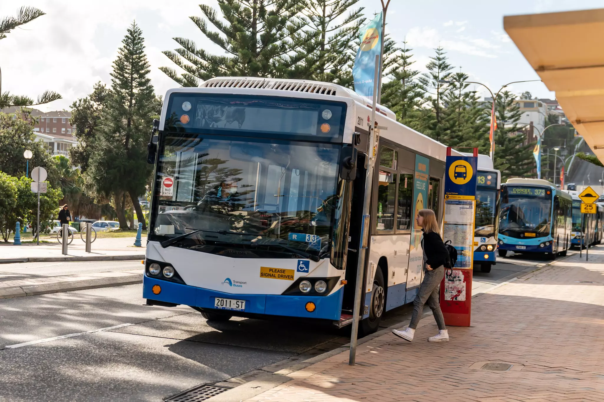 A person walking toward a public bus with other buses parked in the distance on a sunny day.