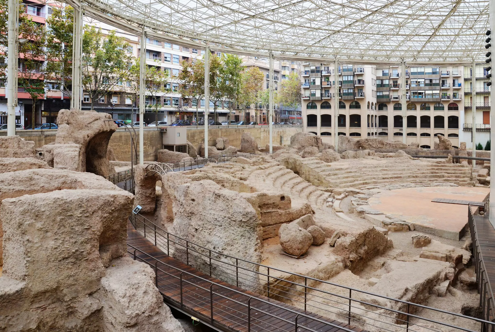 The ruins of an ancient Roman theater with a modern walkway and covered glass roof.