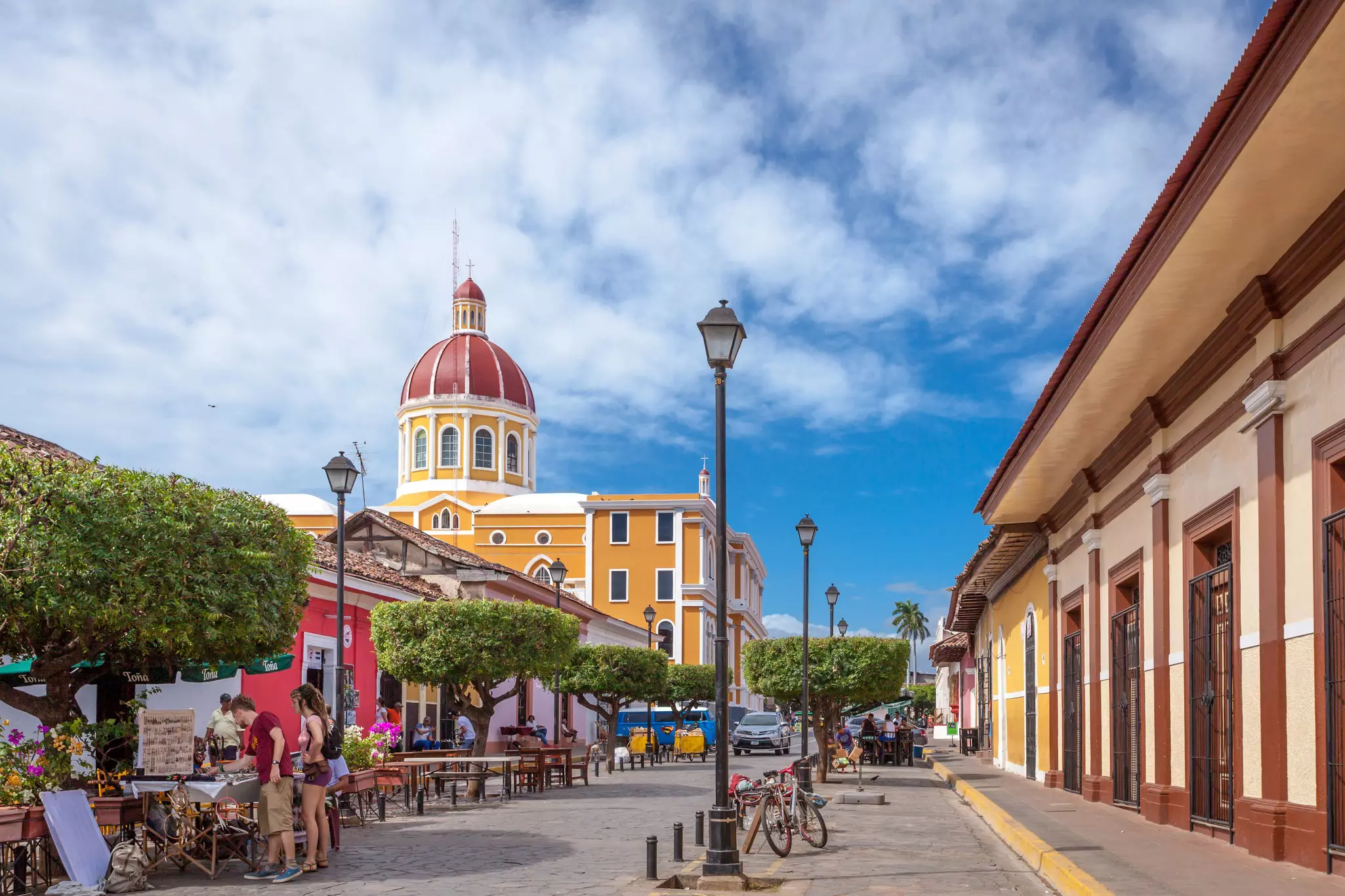 Colonial buildings in pastel shades line a walkway in a town center. A domed building towers above the street.