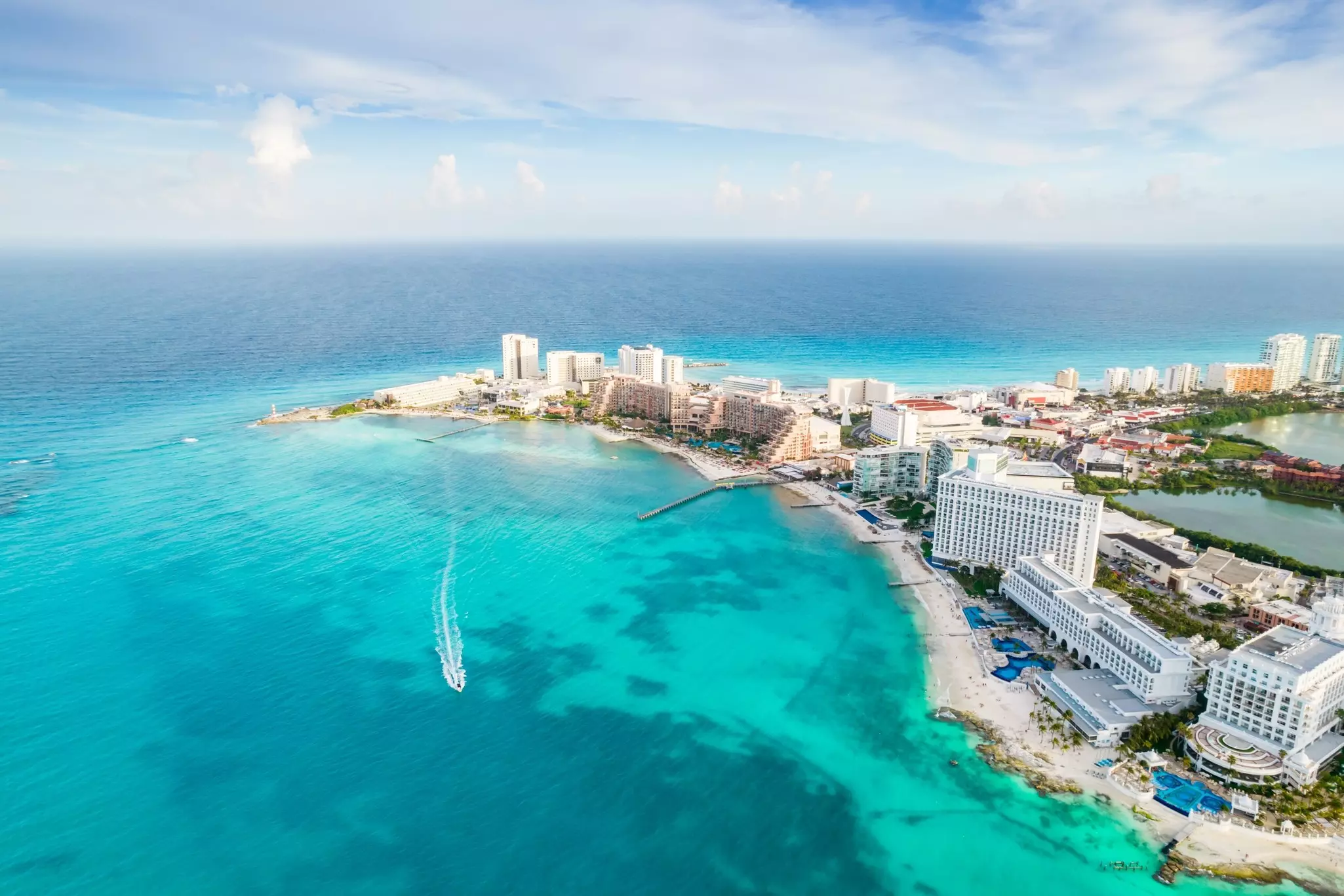 An aerial view of resort hotels on a spit lining a beach, surrounded by blue waters.