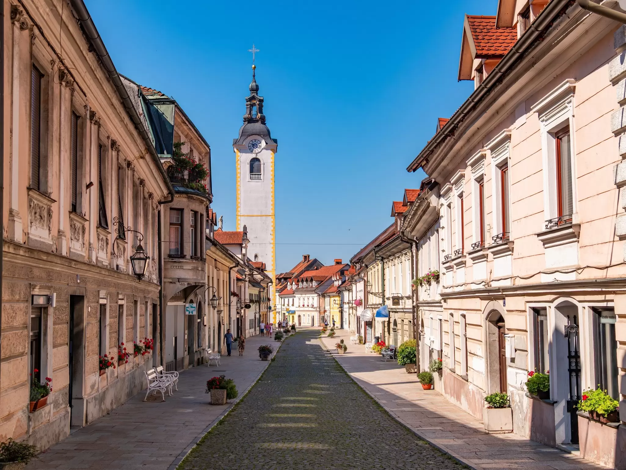 A charming cobbled street lined with stone houses leading to a church tower.