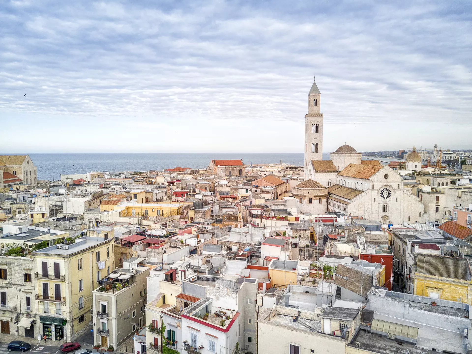 A view of the tightly packed buildings of Bari Vecchia, with the spire of the Basilica di San Nicola and the sea in the distance.