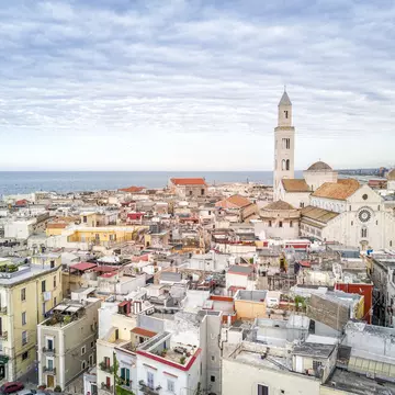 A view of the tightly packed buildings of Bari Vecchia, with the spire of the Basilica di San Nicola and the sea in the distance.