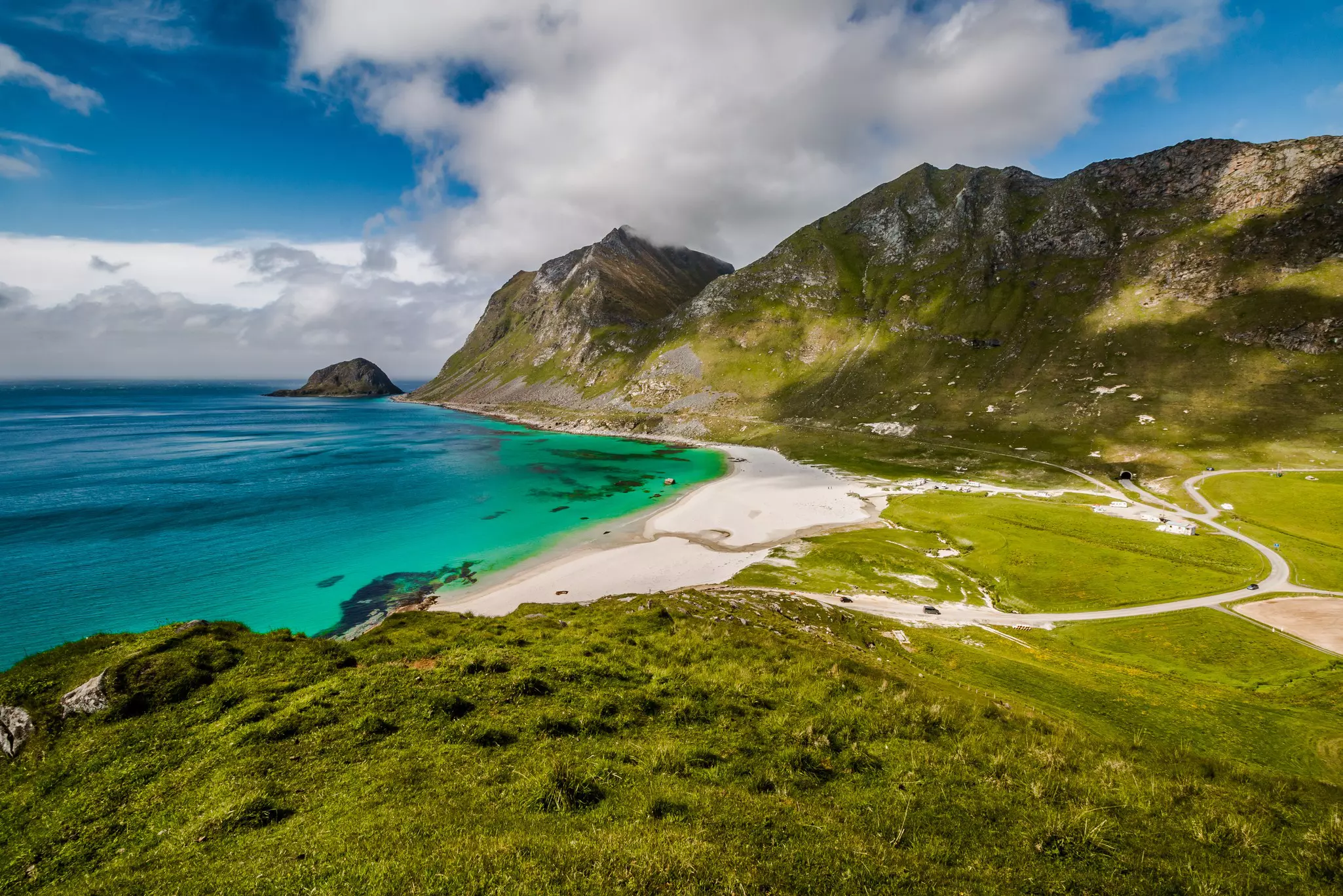 A sandy beach with turquoise waters backed by greenery-covered cliffs in Norway