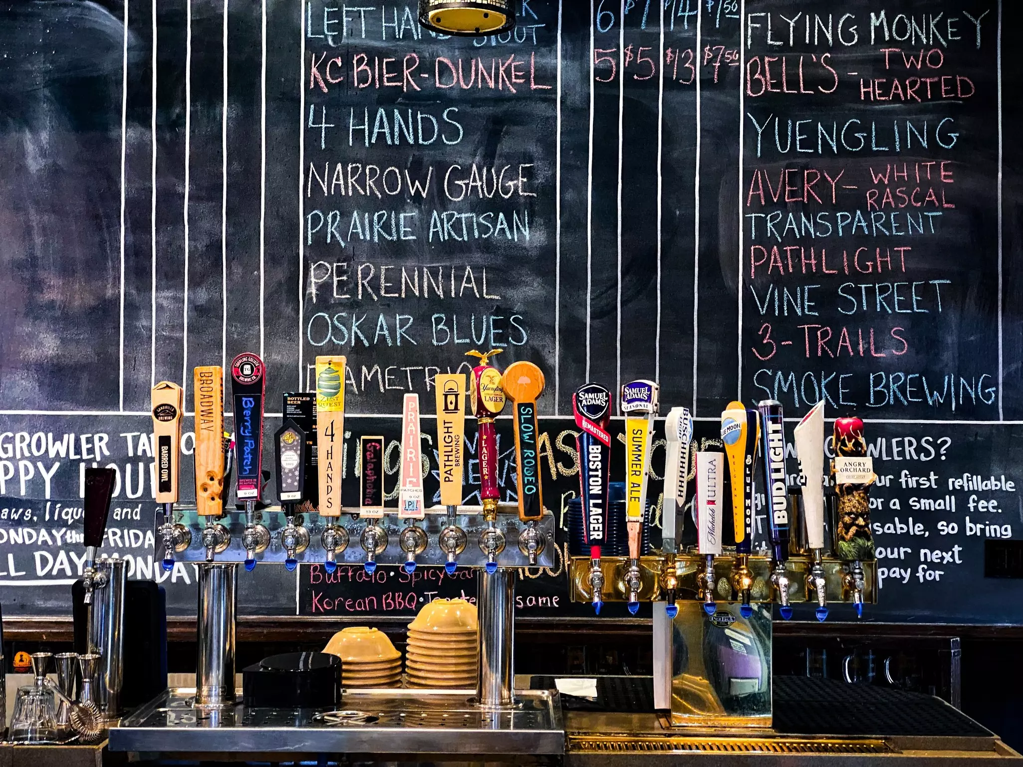 Beer taps at a bar with chalkboard background. Samuel Adams, Michelob, Busch, Blue Moon, Bud Light, Angry Orchard, Yuengling, Pathlight, 4 hands