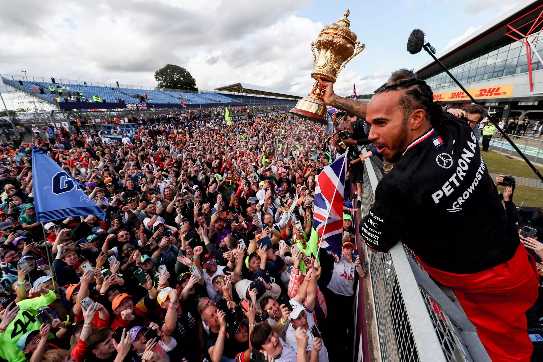 A man holds a trophy high above a crowd of fans who are looking up at him, taking photos and smiling
