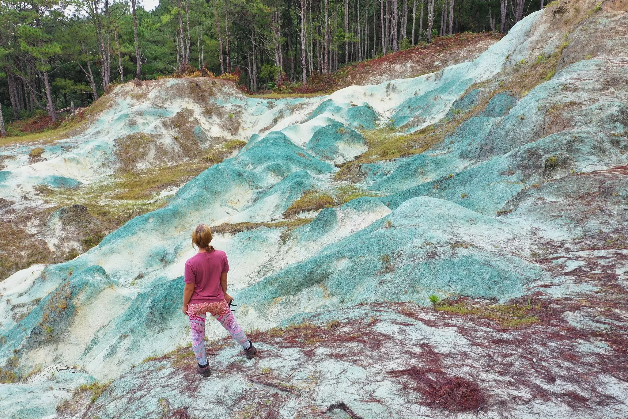 A hiker stands to look over a view of rolling hills that are colored blue due to minerals.