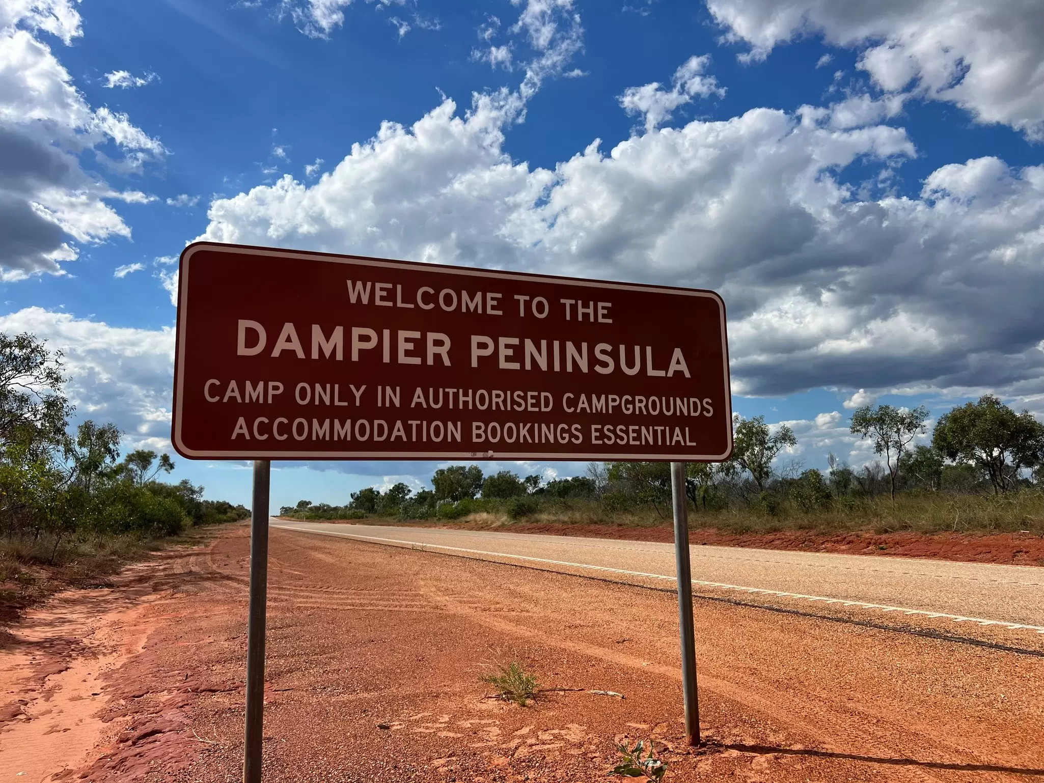 A road sign for the Dampier Peninsula sits beside a highway surrounded by red dirt.