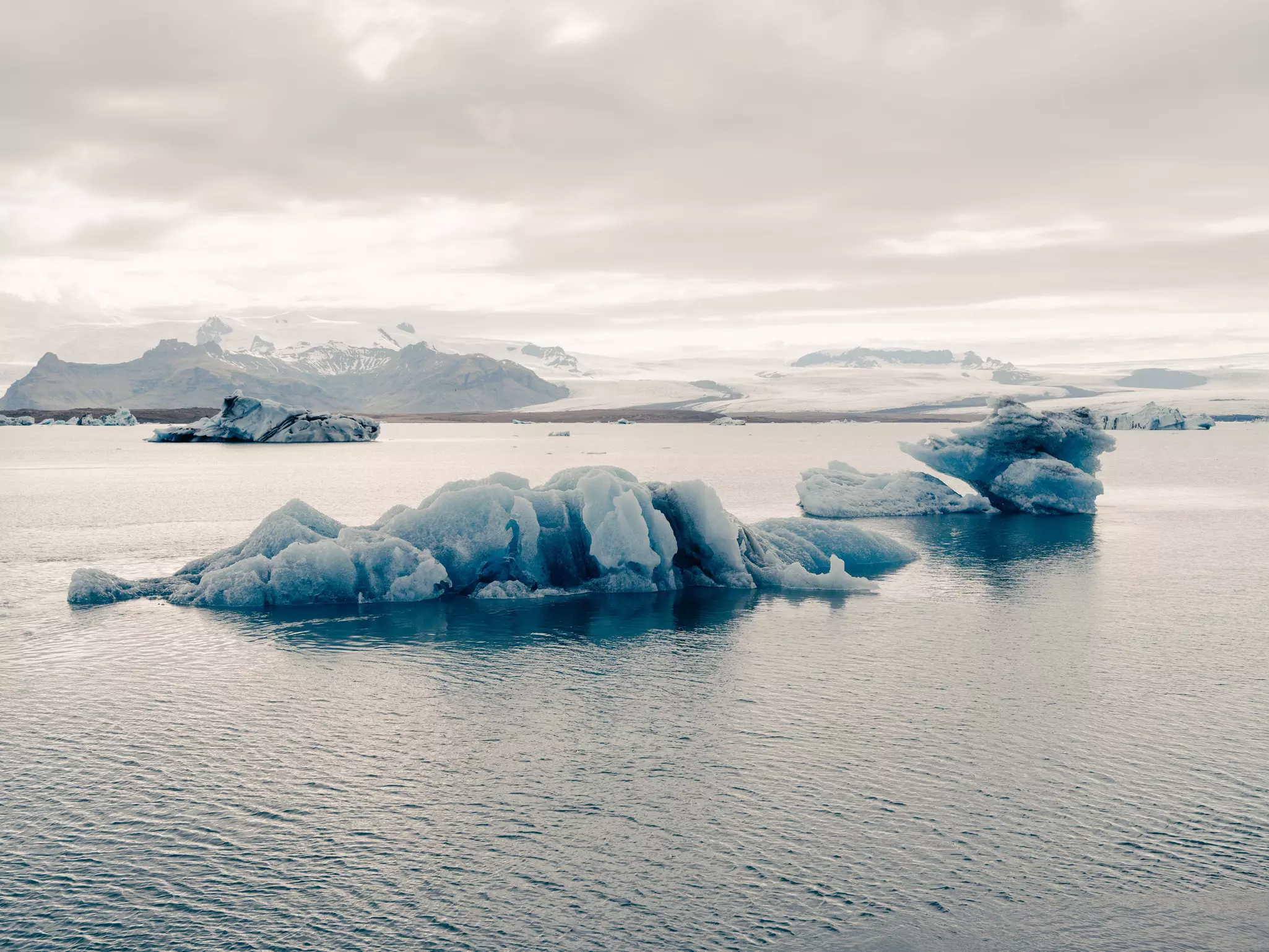 Blue icebergs in a lagoon under cloudy skies.