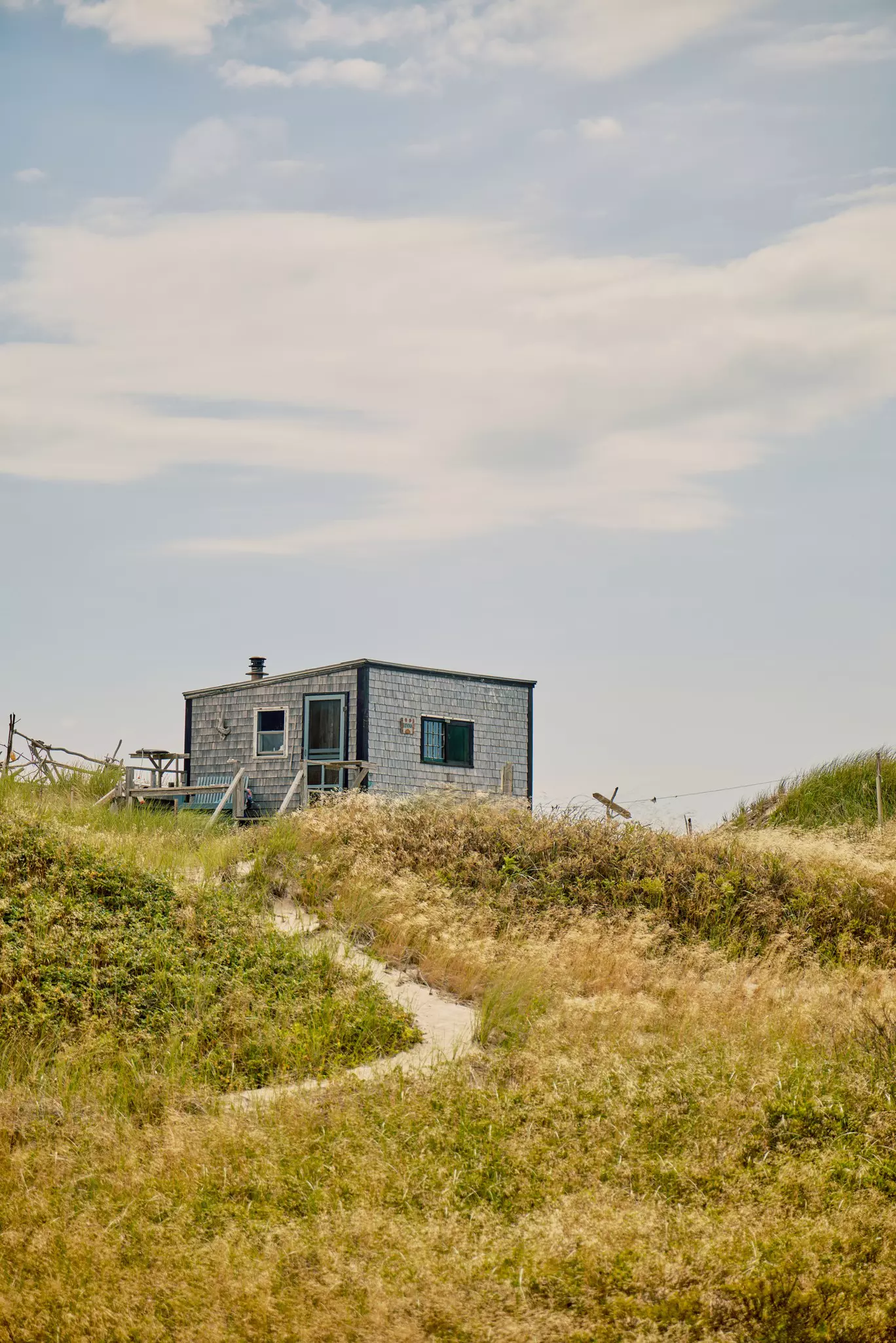 A beach trail leads up to a small seaside shack with two windows and a door visible in the frame