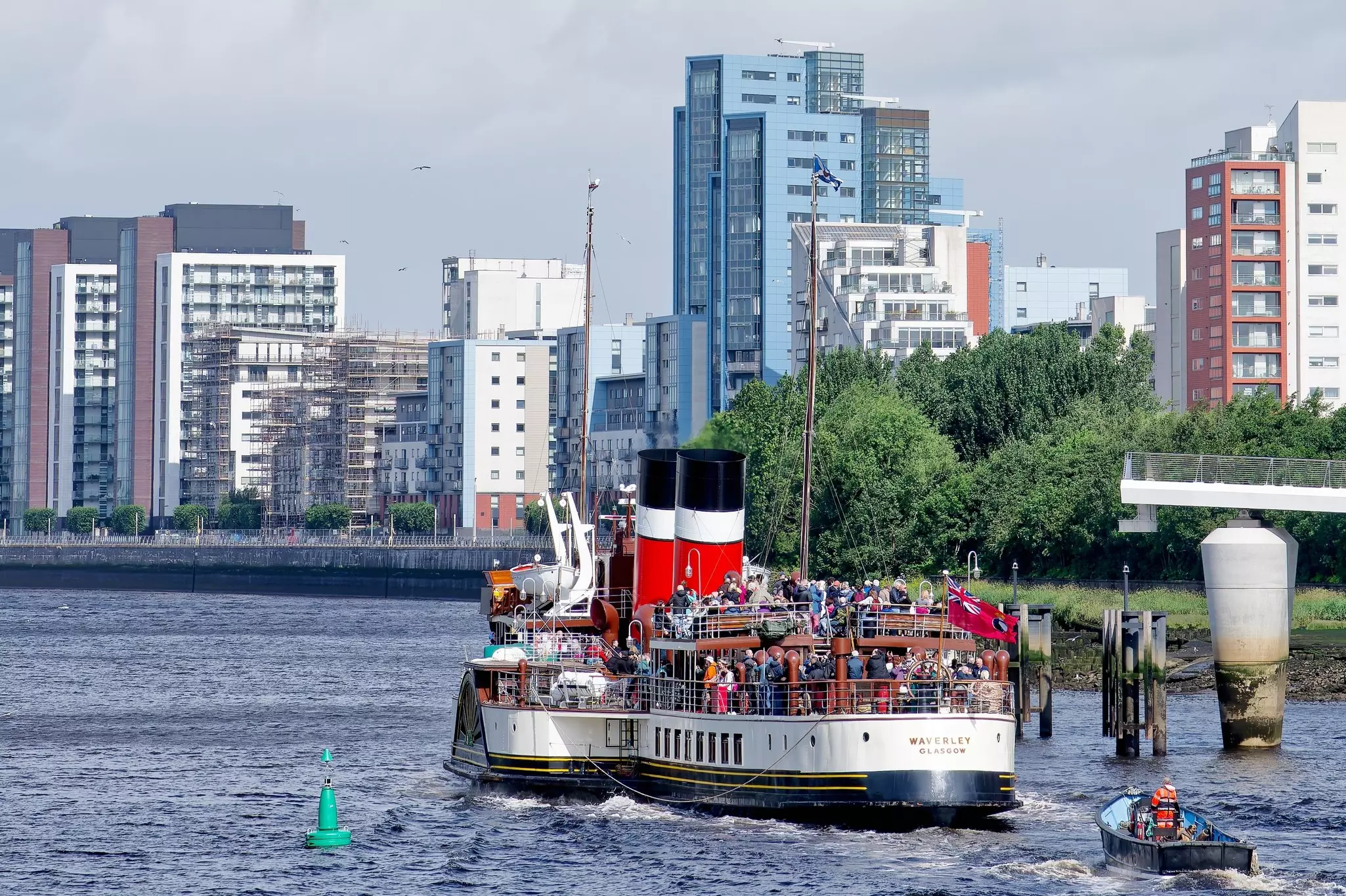 A paddle steamboat with many people on the deck navigates the River Clyde in Glasgow, Scotland.
