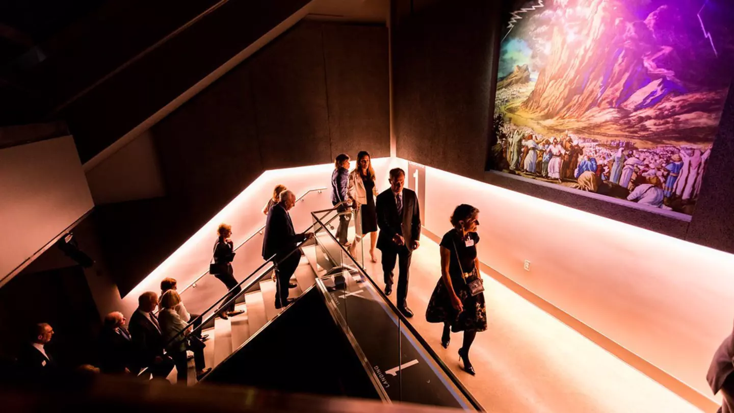 People walking up purple-lit stairs at the Dallas Holocaust and Human Rights Museum