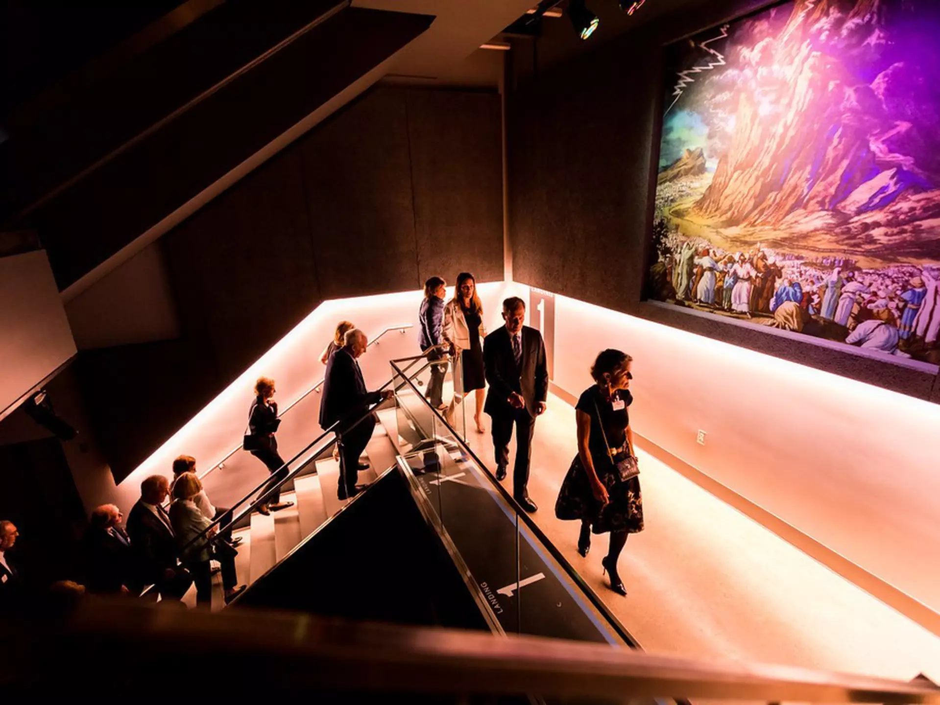 People walking up purple-lit stairs at the Dallas Holocaust and Human Rights Museum