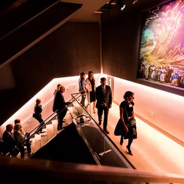 People walking up purple-lit stairs at the Dallas Holocaust and Human Rights Museum