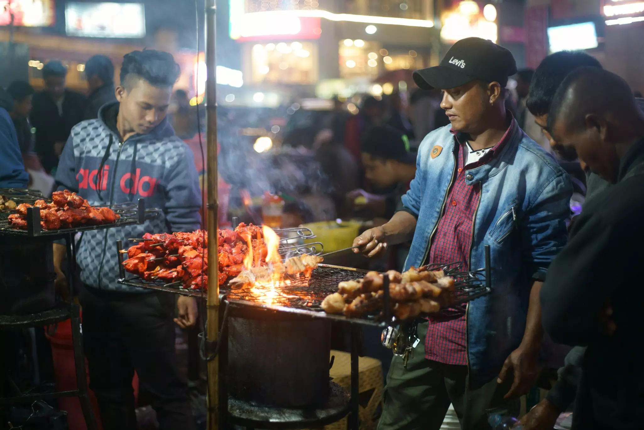 A street-food vendor preparing meat kebabs over a grill at a night market.