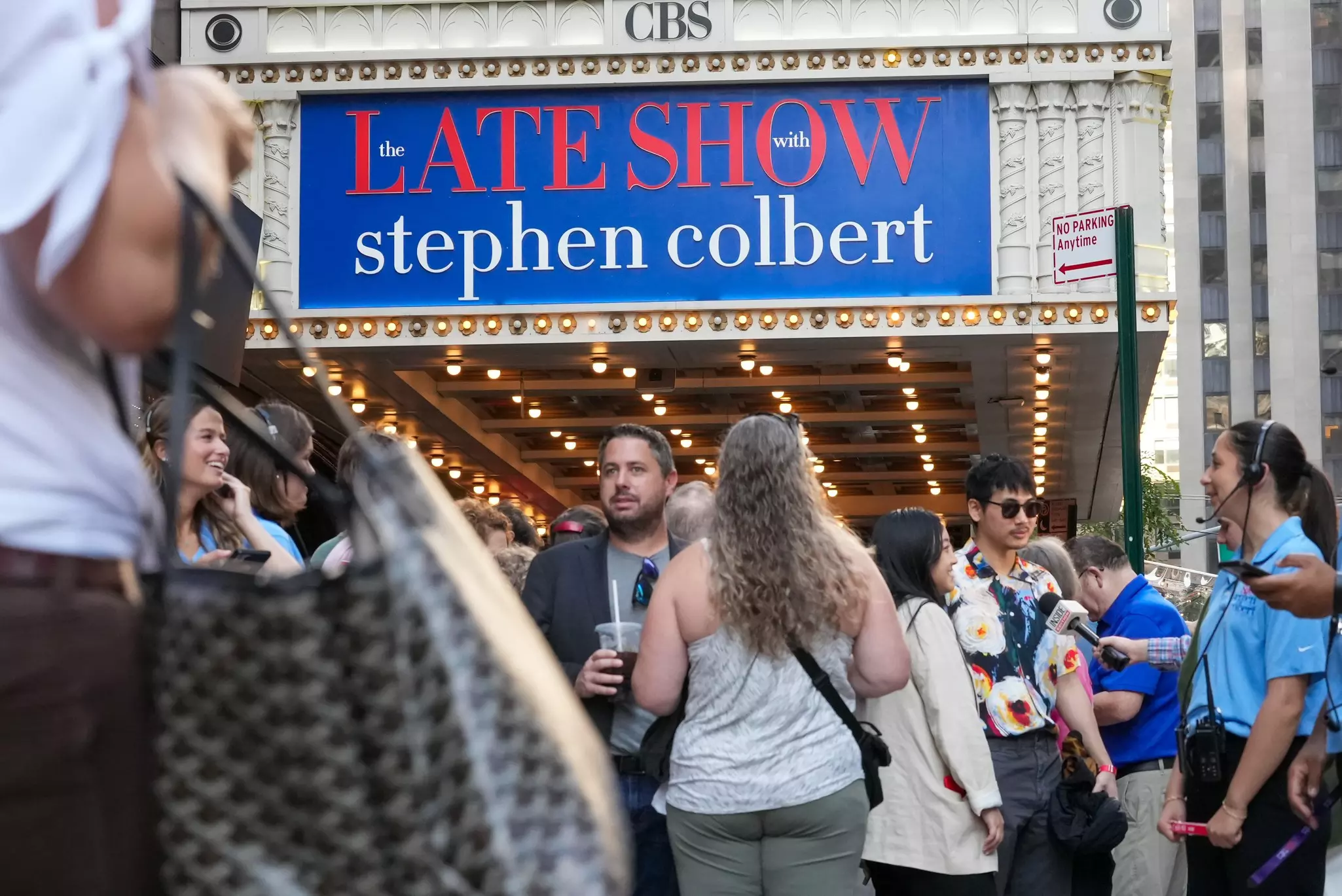 People queue outside the marquee of a theater in a city street.