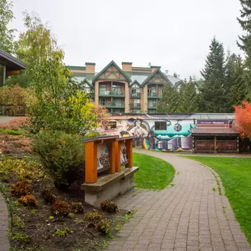 A curving brick path through a garden leads to a low mural-painted building with a Whistler Museum sign