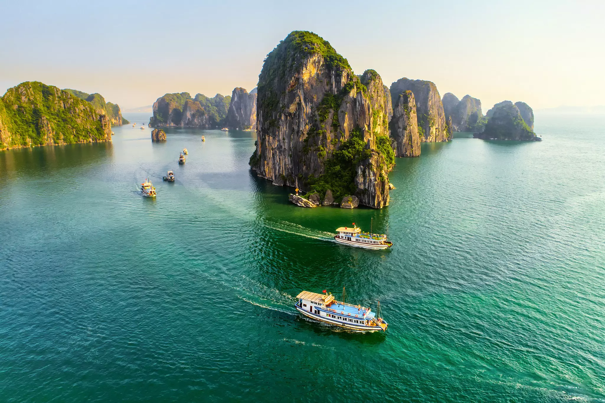 Boats sail past rocky islands in a bay of green water in Vietnam.