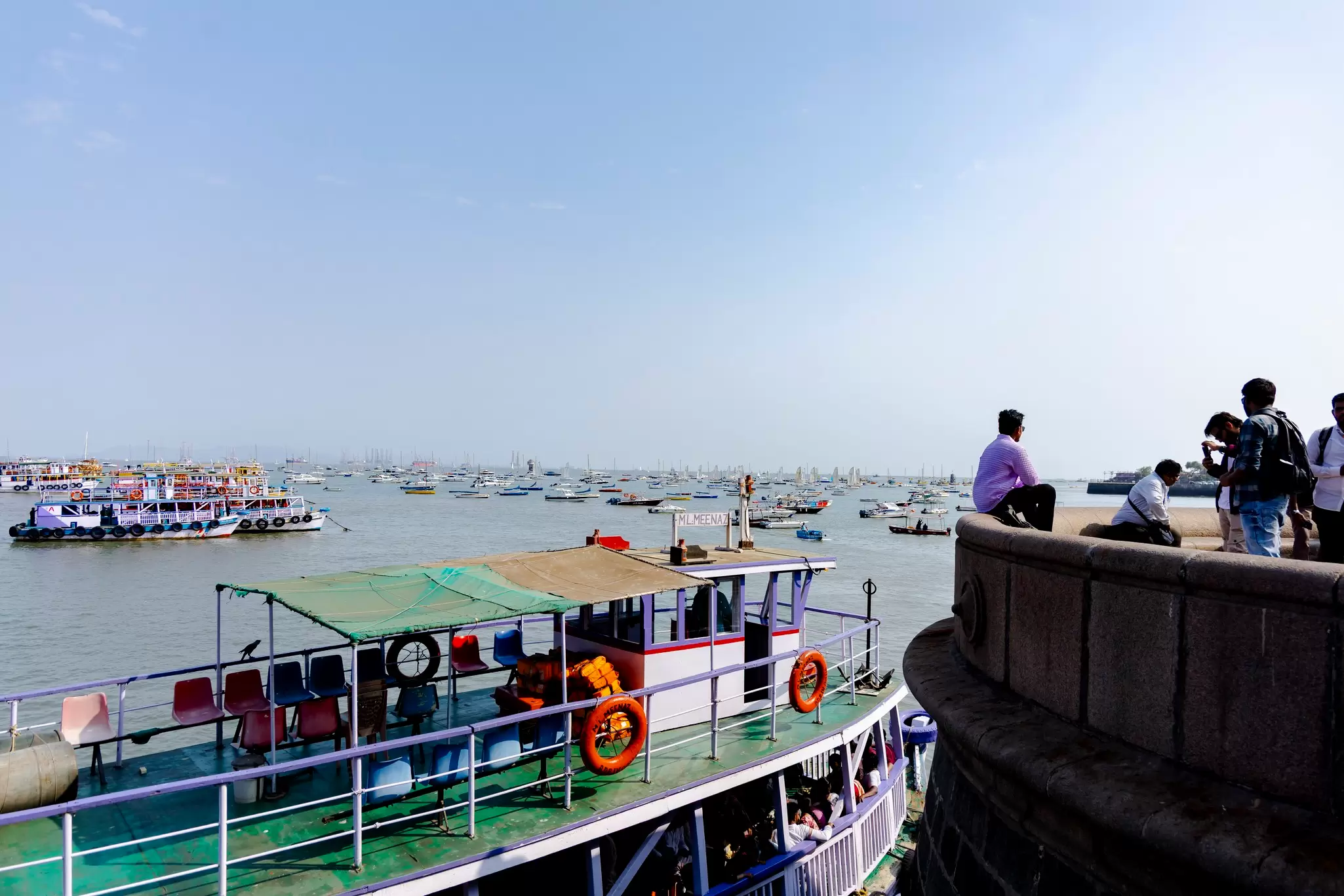 Colorful ferries on the water leaving the Gateway of India, Mumbai for Elephanta Island, a group of men on the right