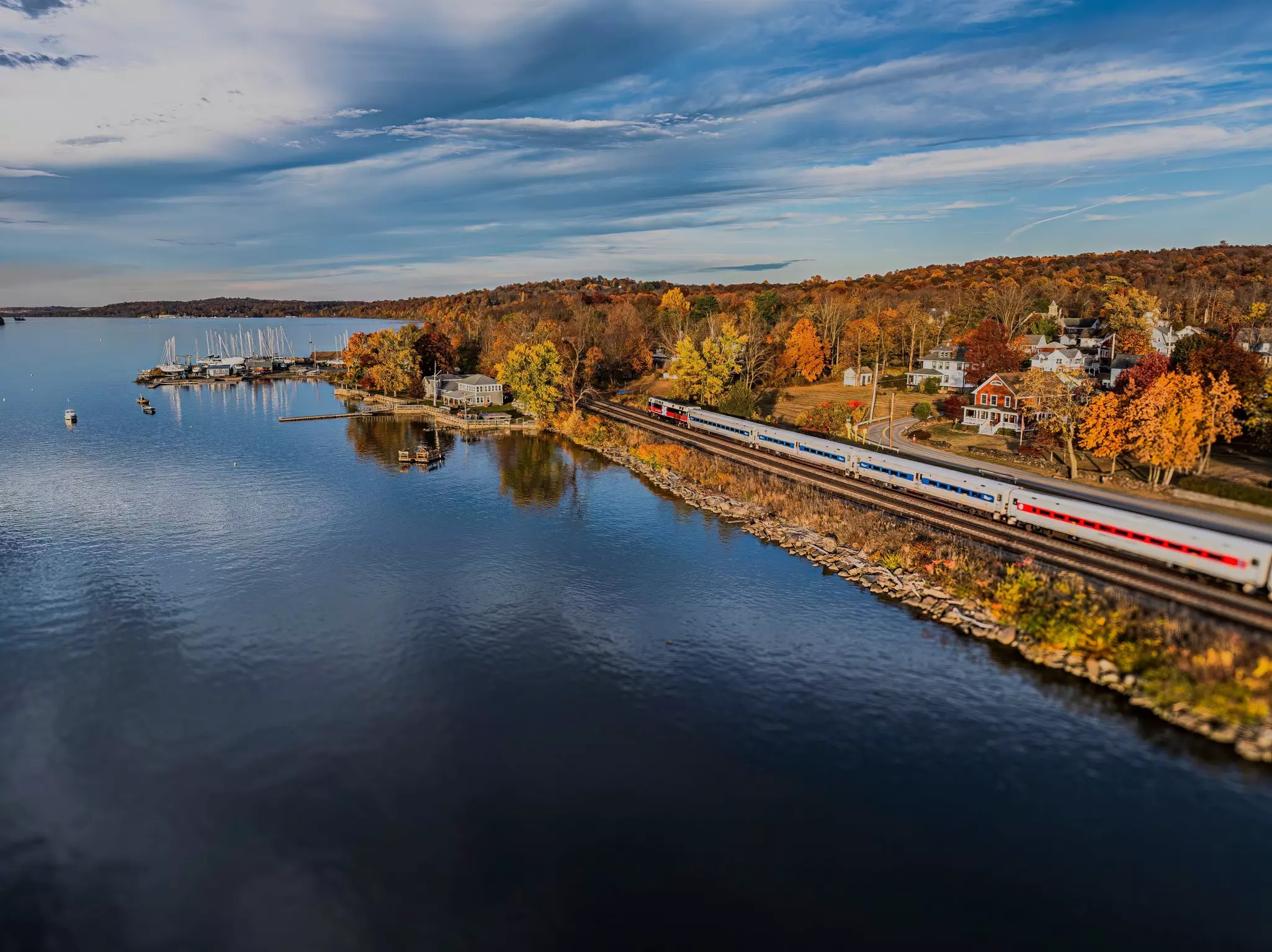 A train speeds along beside a river lined with golden trees in the fall.
