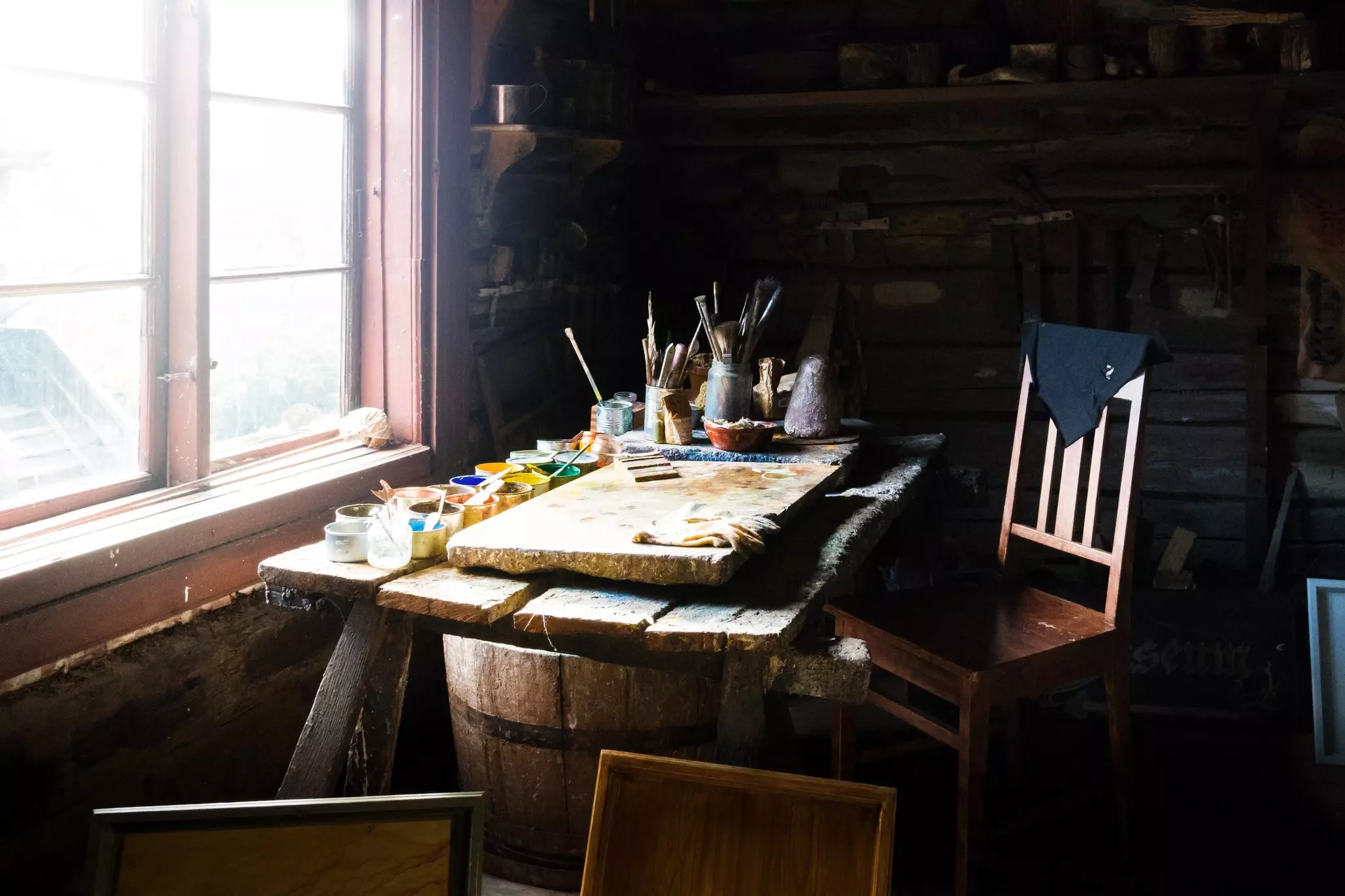 Art supplies including colors and brushes sit on a desk by a window in a traditional painter’s workshop.