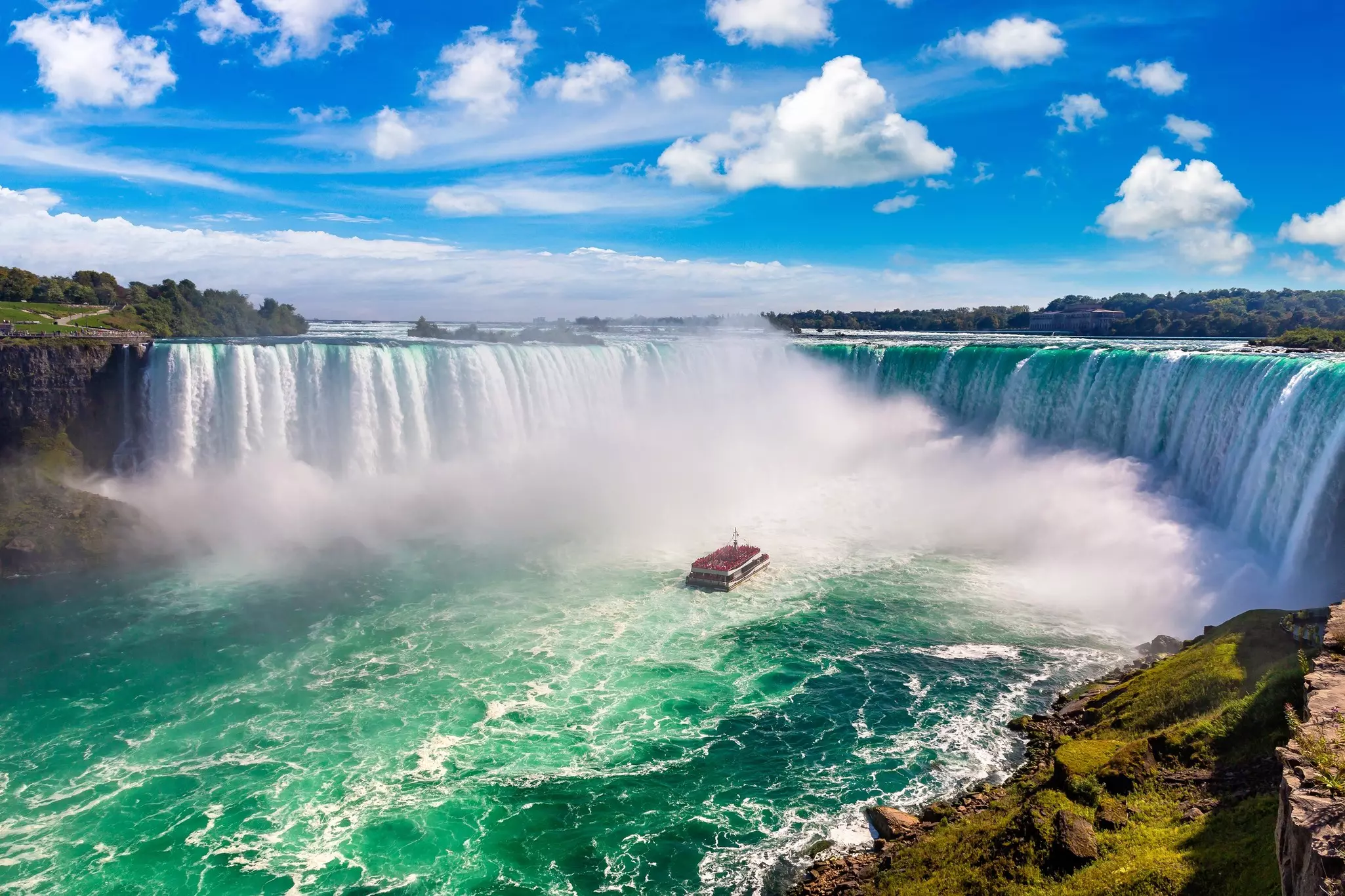 A vast horseshoe-shaped waterfall cascading wildly down into a huge pool. A tourist boat floats in the mist in the center.